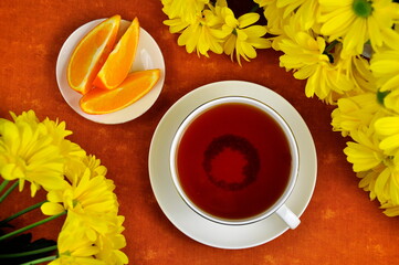 A mug of black tea, yellow chrysanthemums and orange slices.