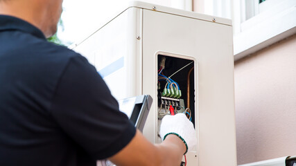 Close up technician hand using measuring equipment checking electric current voltage at circuit breaker on outdoor air compressor unit after installation and air conditioner services maintenance