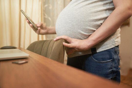 Pregnant woman at home with phone stands near a table with computer, concept: online shopping. High quality photo