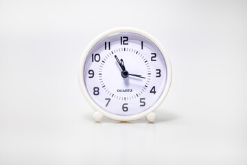 Small white alarm clock show the running time. A modern clock with white frame. Smile face of a clock. Close up on a white plastic watch with second pointer on white background. Five to twelve 
