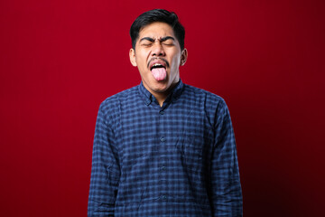 Fototapeta premium Young handsome asian boy wearing casual shirt standing over red background sticking tongue out happy with funny expression.