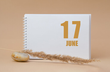june 17. 17th day of the month, calendar date.White blank sheet of notepad, stones, dry sprig of grass, on beige background.Summer month, day of the year concept
