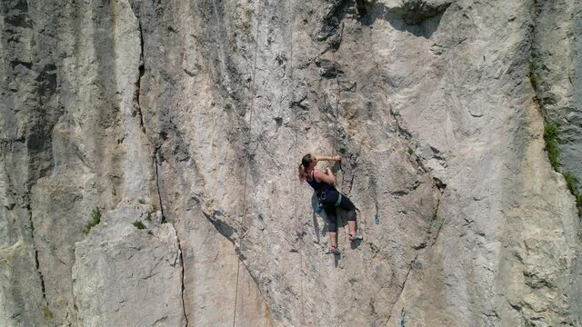AERIAL: Drone point of view of an athletic woman learning to top rope climb in Slovenia. Unrecognizable athletic female top rope climbs in Crni Kal on a sunny spring day. Extreme outdoor sport.