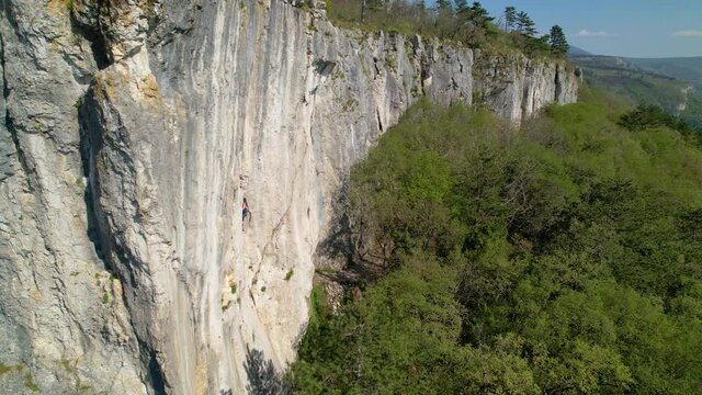 AERIAL: Drone point of view of a fit Caucasian female climber top roping up a towering cliff in Crni Kal, Slovenia. Spectacular rural scenery surrounds athletic young woman learning to top rope climb.