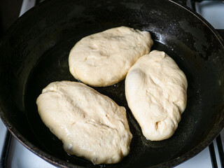 three raw cooked pies are fried in oil in pan