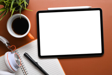 Digital tablet with empty screen, stylus pen, notebook, headphone and headphone on brown leather.