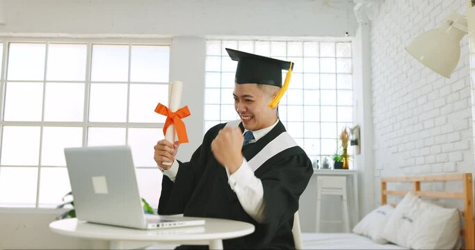 Happy excited college or university student sitting at desk with laptop, holding diploma and celebrating success 