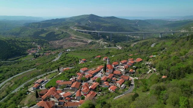 AERIAL: Flying above a quiet town near a breathtaking highway bridge crossing the green valley in Slovenia. Scenic drone shot of the Crni Kal village overlooking the spectacular highway viaduct.