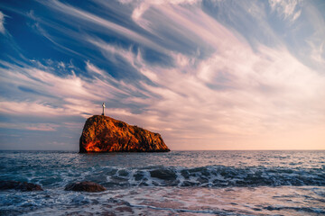 Bright sea sunset. The waves crash into the rock, lit by the warm sunset, sand and pebbles, volcanic basalt as in Iceland. Sea wave breaks into splashes and white foam. Never-ending beauty of nature