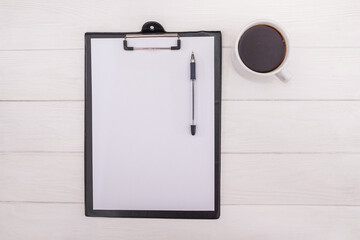 tablet with a white sheet with a pen and a cup of coffee on a white wooden background with boards. View from above.