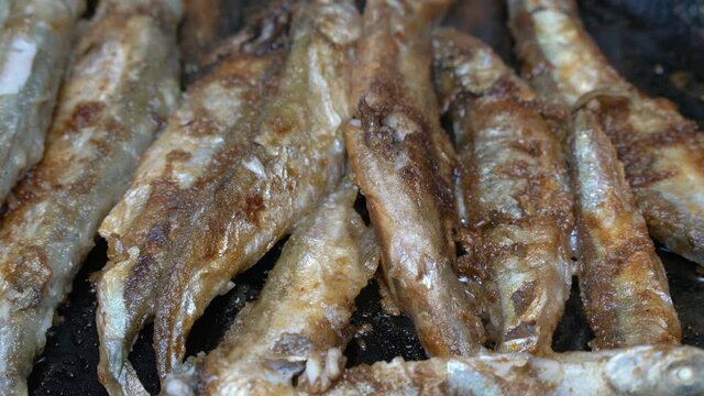 Close-up view of cooking frying capelin fish in iron pan. Broiled caplin fish - unhealthy Asian food where entire fish, from head to tail, roe and bones can be enjoyed as an appetizer or garnish.