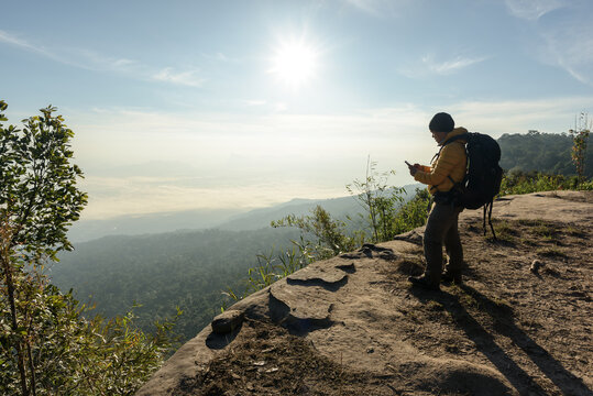 Man traveler is using digital phone on cliff with beautiful landscape sunset in national park, Thailand.