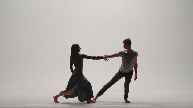 Elements of modern choreography, contemporary performed by a young couple of dancers on a white studio background. Man and woman dance passionately, expressing their feelings in a dance. Slow motion.