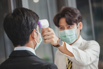 man with a thermometer measures the temperature of employees in protective masks. fever measures using digital thermometer check temperature measurement on the forehead. Covid-19, 