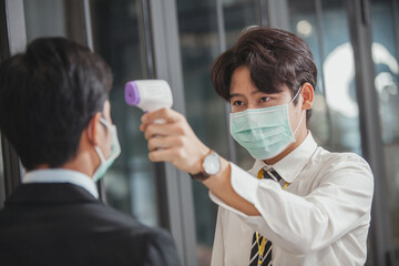 man with a thermometer measures the temperature of employees in protective masks. fever measures using digital thermometer check temperature measurement on the forehead. Covid-19, 