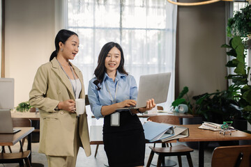 Young Asain businesswoman working together in office. Two women with laptop in open space office. Business concept. Business project team working together at meeting room at office