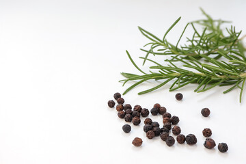 Black pepper grains, fresh rosemary herb on white background.
