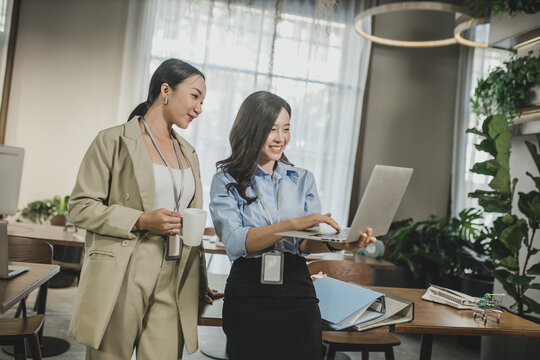 Young Asain businesswoman working together in office. Two women with laptop in open space office. Business concept. Business project team working together at meeting room at office