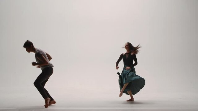 Elements of modern choreography, contemporary performed by a young couple of dancers on a white studio background. Man and woman dance passionately, expressing their feelings in a dance. Slow motion.