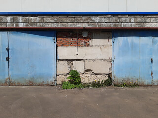 Industrial Zone. A blue iron gate in a concrete block wall. Ruin. Summer.