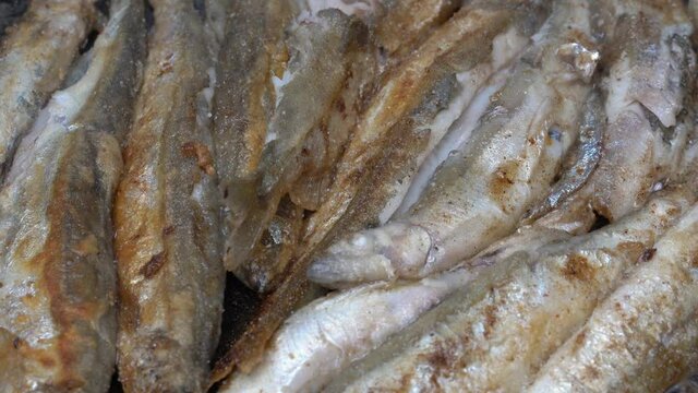 Close-up view of cooking frying capelin fish in pan. Broiled caplin fish - nutritious Asian cuisine where entire small fish, from head to tail, roe and bones can be enjoyed as an appetizer or garnish.