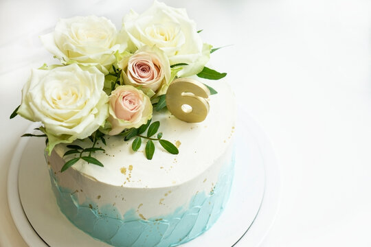 wedding  anniversary   cake  decorated  white and turquoise cream with natural roses and  gold number 6 on white background  with space for trxt . Birthday cake concept  .