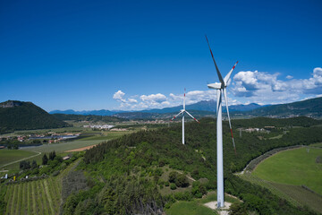 Fototapeta na wymiar Windmill surrounded by olive trees, vineyards, Alps. Wind turbine in Italy. Wind generators in the mountains of Italy. Wind farm in the Alpine nature. Wind turbine in Affi, Lake Garda.