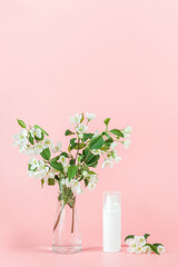 One white blank cosmetic tube bottle and flower, blooming branch on pink background. Natural Organic Spa Cosmetic Beauty Concept. Mockup Front view
