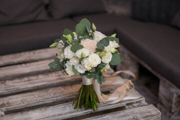 Beautiful bridal bouquet of white flowers and greenery, decorated with long silk ribbon lies on a wood table. Copy space