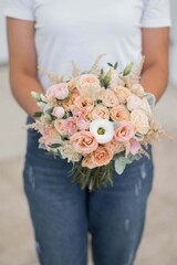 Pink wedding bouquet, composed of roses, freesias, peonies, hypericum, astilba and eucalypthus, in florist hands.