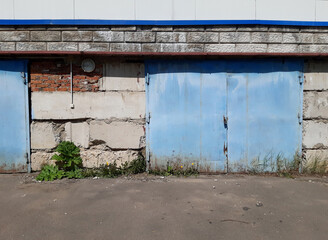Industrial Zone. A blue iron gate in a concrete block wall. Ruin. Summer.