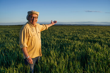 Senior farmer is standing in his growing wheat field. He is happy because of successful sowing.