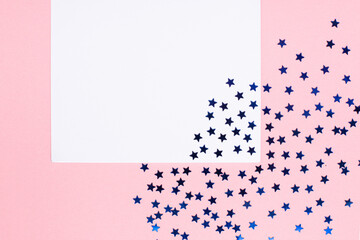 blank white sheet of paper on a pink background with blue sparkles in the form of stars close-up. the place for your mockup and text