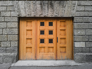 Smooth wooden closed doors in the facade of the wall of the building with stone blocks.