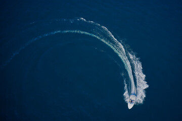 Top view of a white boat sailing in the blue sea. A boat with a motor on blue water in a turn. Top...