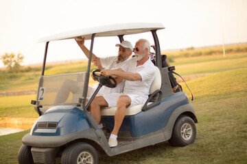 Two older friends are riding in a golf cart.