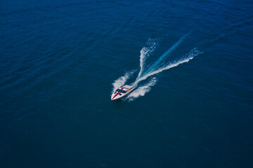 Drone view of a boat sailing across the blue clear waters. Top view of a white boat sailing in the blue sea. Aerial view luxury motor boat.