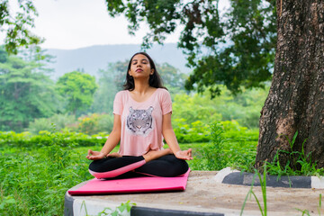 Young and fit Indian woman practising yoga on a mat in nature