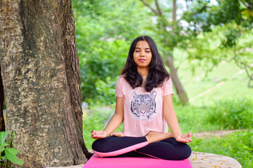 Young and fit Indian woman practising yoga on a mat in nature