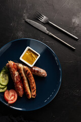grilled sausages with vegetables on a blue plate on a black background