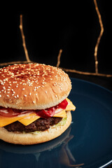 burger on a blue plate on a black background with a golden twig overhead side view