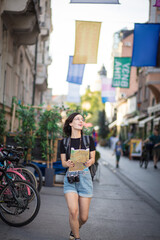  Young woman tourist running trough street with map in hands.