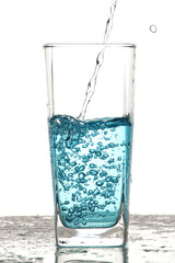 Pouring blue water into glass against light white background. Fresh water a glass with bubbles. Water drop on the side glass. Wet floor.