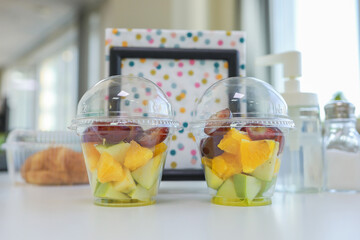 wo plastic cups with sliced fruit. Apple, orange, grape. Fruit office breakfast on the table. Blurred background. Beautiful polka dot napkins on the background.