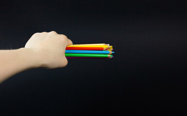 A woman's hand holds an armful of colored drawing pencils in her fist. Black background.