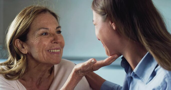 Cinematic shot of happy smiling grandmother is giving affective hug to granddaughter as sign of love and care while sitting on sofa at home. Concept: life, grandparents, generation, love, care, family