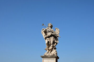 Fototapeta premium marble sculpture of an angel holding a hammer with the blue sky in the background in the city of rome, sant angelo castle bridge, italy