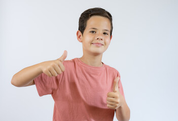 Cheerful smiling little boy standing over white background and showing thumbs up