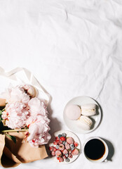 Fototapeta na wymiar a cup of coffee, berries, macaroons and peony flowers on the bed