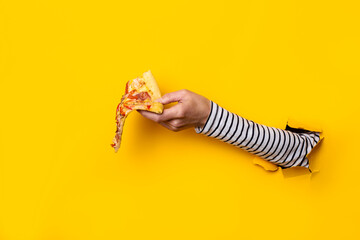 female hand holds a slice of fresh hot pizza on a torn yellow background